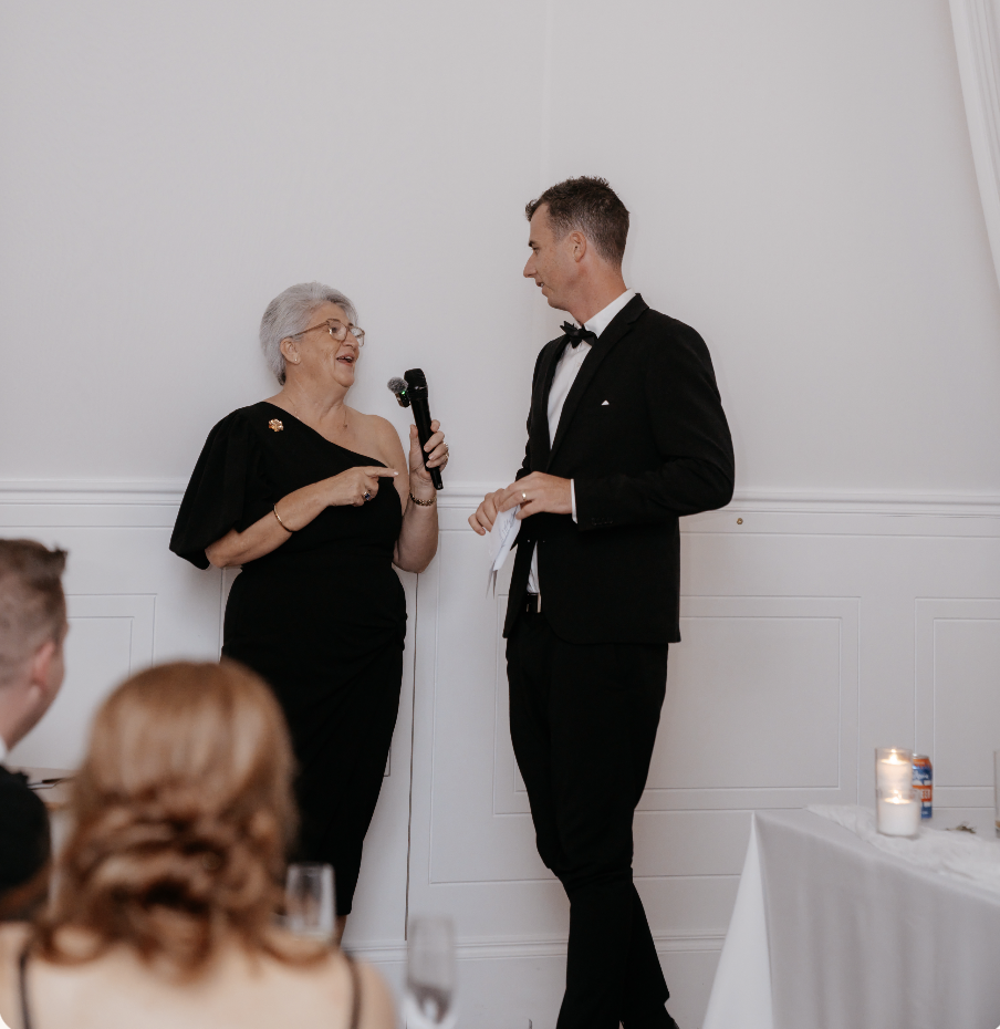 April Daley-Holmes as Master of Ceremonies speaking with the groom at a wedding reception
